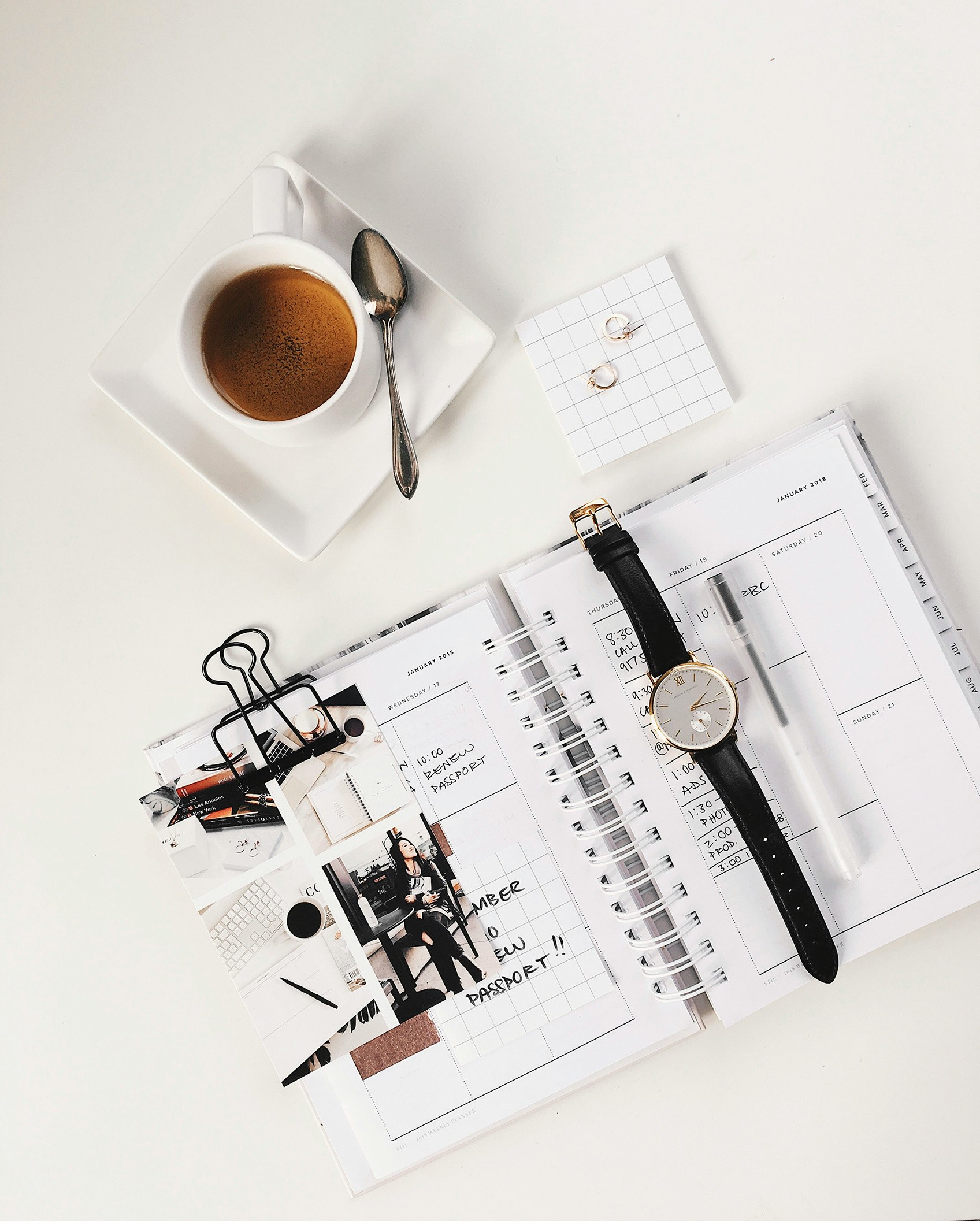 analog watch on top of book beside white ceramic teacup with teaspoon